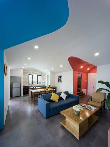 Phòng khách và bếp ăn được bố trí mở khiến không gian càng trở nên thoáng rộng. Chiếc sofa màu xanh đặt quay lưng lại với khu bếp có chức năng là bức tường ngăn cách giữa hai khu vực.