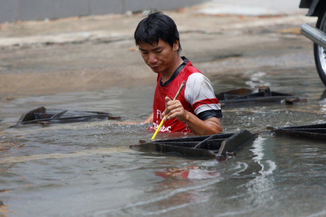 Một nhân viên công ty truyền cáp leo xuống cống ngầm để lắp đặt đường cáp trong khi nước ngập sâu tới phần ngực - Ảnh: LÊ PHAN