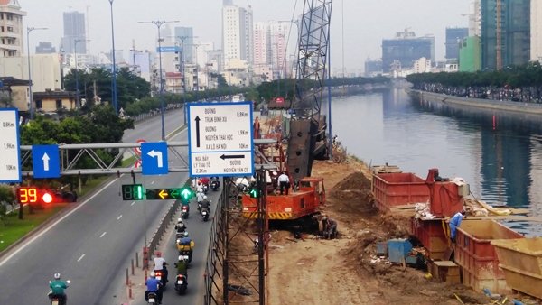 Tại chân cầu Nguyễn Văn Cừ (Q.1), công trình xây dựng cầu nối đường Võ Văn Kiệt với cầu Nguyễn Văn Cừ đang được rào chắn, lấn chiếm mặt đường.