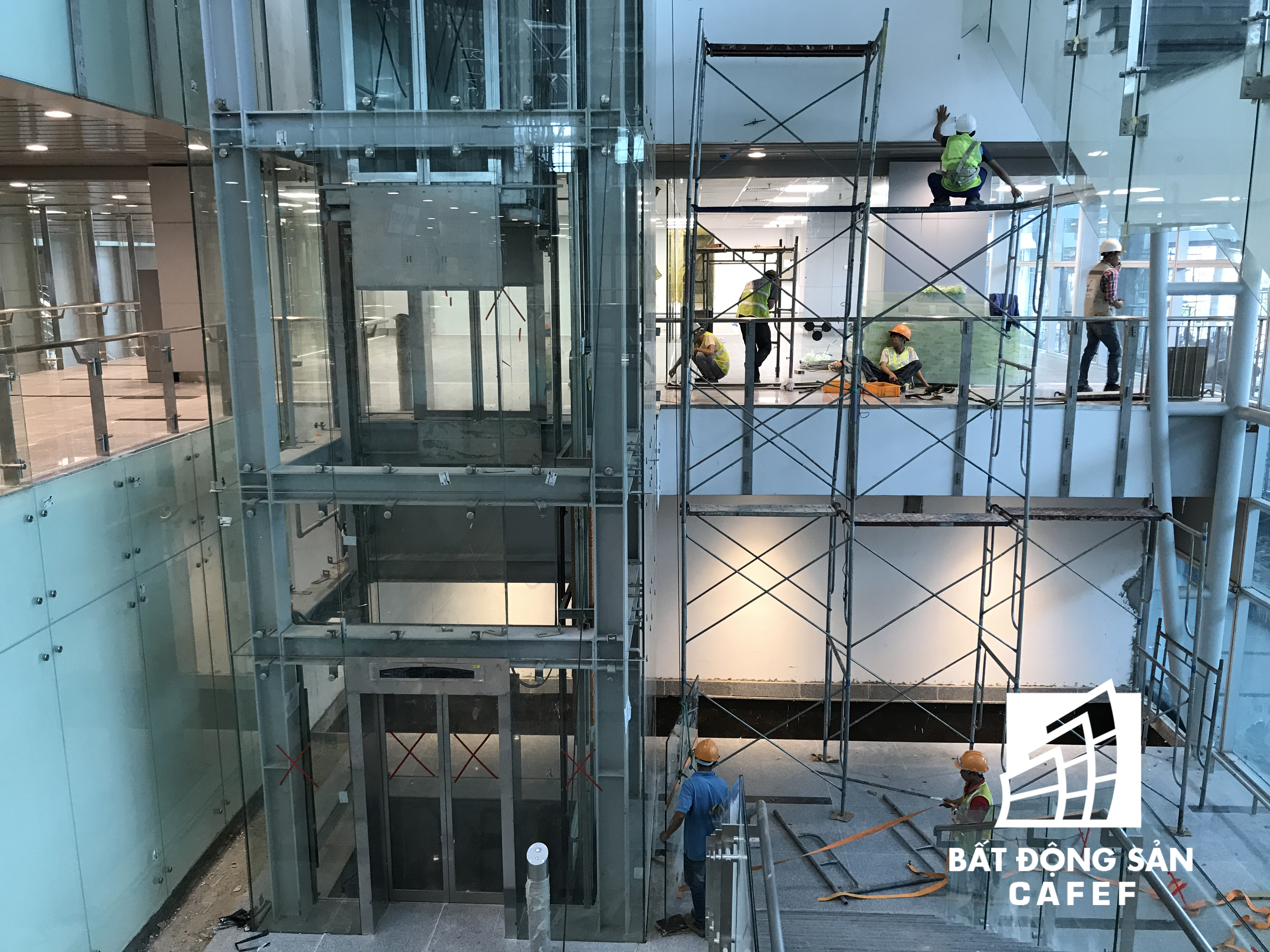 Đội ngũ công nhân đang lắp kính và vận hành thử hệ thống thang máy bên trong nhà ga.