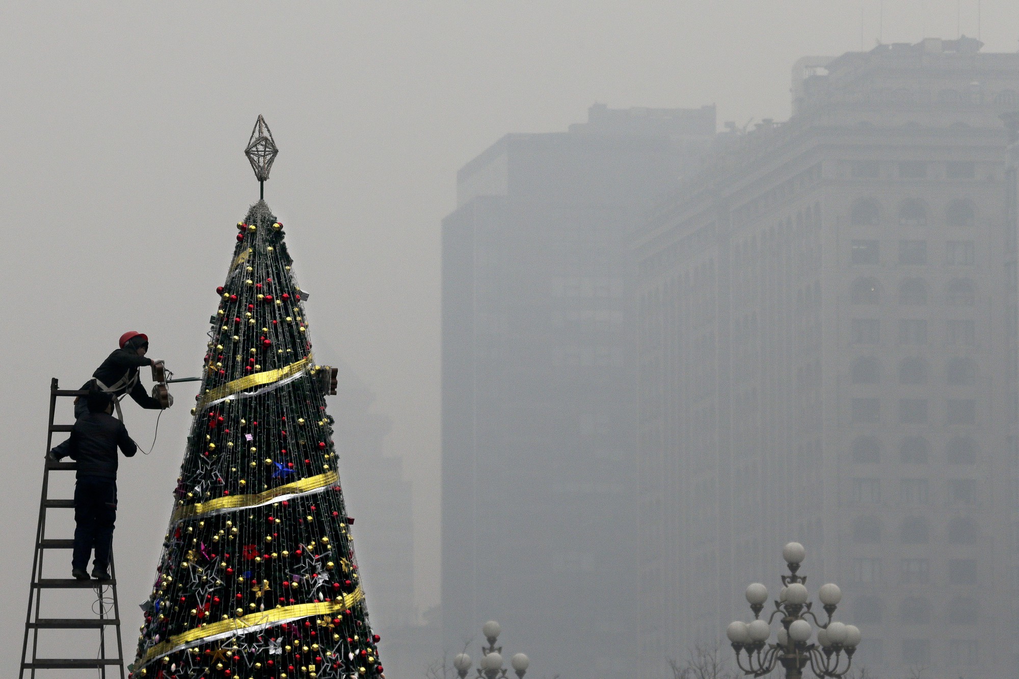 Một người thợ đang tu sửa cây thông Noel khổng lồ tại thành phố Bắc Kinh giữa bầu không khí không được trong lành cho lắm.