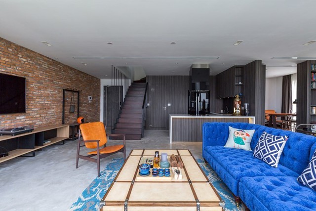 Không gian phòng khách thoáng sáng và tràn ngập ánh sáng tự nhiên nổi bật với ghế sofa xanh giữa nền tường màu tối.