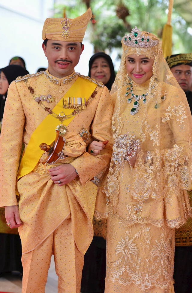Hoàng tử Brunei Abdul Malik và vợ, Dayangku Raabiatul Adawiyyah Pengiran Haji Bolkiah trong lễ kết hôn năm 2015. Trang phục của cô dâu chú rể được thiết kế theo truyền thống của đất nước. Cô dâu nổi bật với bộ trang sức và vương miện bằng đá quý.