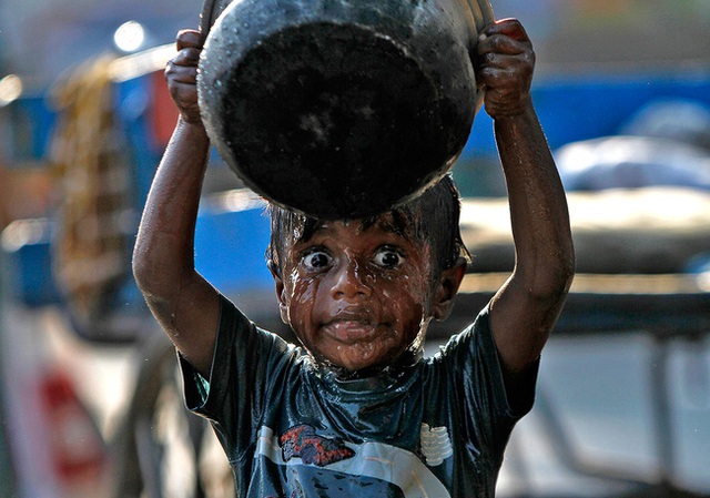 Bé trai tắm ven đường bằng xô nước ở thành phố Chennai, Ấn Độ.