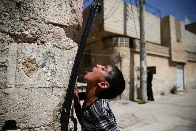 Một cậu bé uống nước từ một đường ống trong thị trấn bị bao vây bởi quân phiến loạn của Douma, phía đông Damascus, Syria.