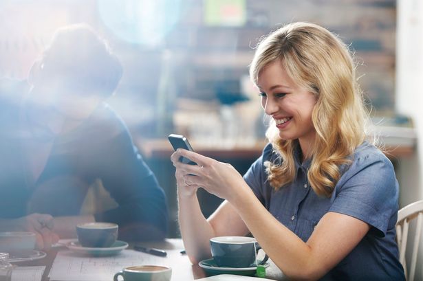 woman-smiling-using-her-phone-in-a-coffee-shop-1474803481276.jpg