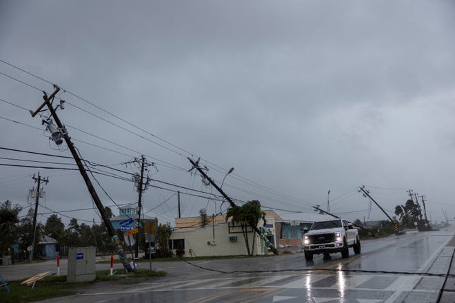 A motorist drives past broken utility poles taken down by strong wind gusts as Hurricane Milton approaches Fort Myers, Florida.