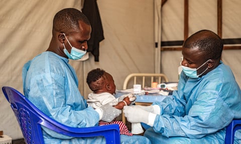 Two medics in scrubs treat a young child in the Democratic Republic of the Congo