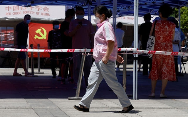 Một người phụ nữ đi ngang qua hàng dài người chờ lấy mẫu xét nghiệm Covid-19 tại Bắc Kinh. Ảnh: Reuters.