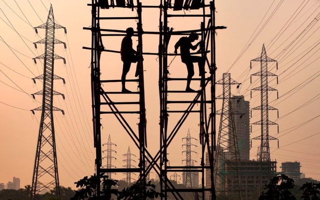 Người lao động làm việc bên cạnh cột điện ở Mumbai, Ấn Độ. Ảnh: Reuters