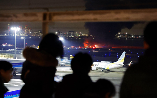 Người dân đứng nhìn chiếc máy bay Japan Airlines bốc cháy từ một tòa nhà ở sân bay Haneda ở Tokyo vào ngày 2-1. Ảnh: Kyodo